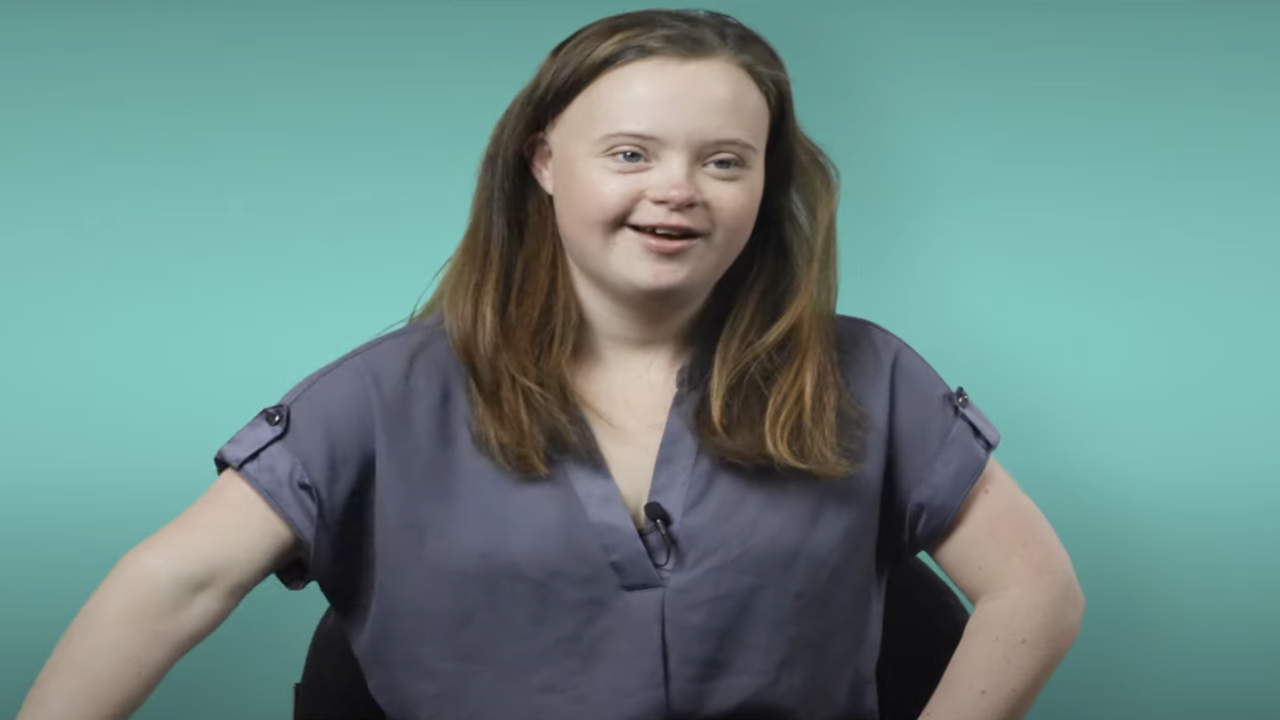 Ashleigh, a young person with Down syndrome smiling and looking at the camera.